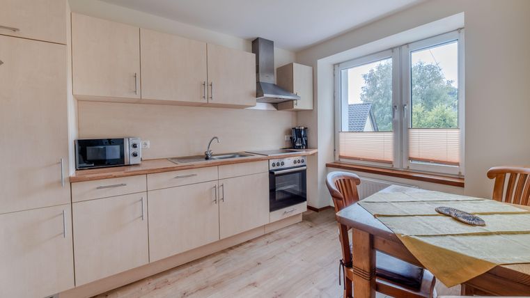 Eine moderne Küche mit hellen Holzschränken und einem großen Fenster. Es gibt einen Esstisch mit Stühlen und verschiedene Küchengeräte.