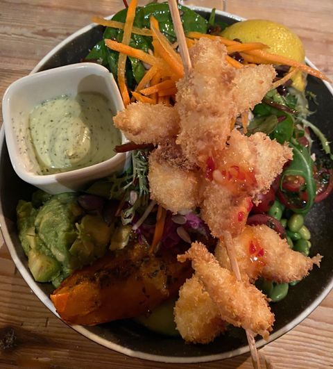 Een kleurrijke salade met gepaneerde garnalen en een kruidendressing. Daarbij zijn er verse groenten en een schijfje citroen.