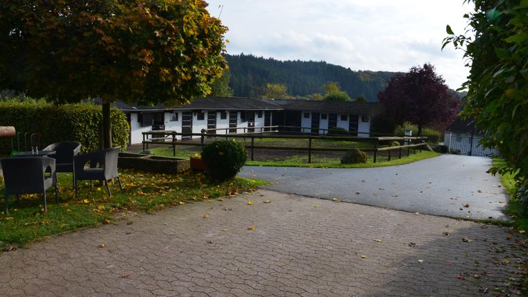 Ein freundliches Anwesen mit einem gepflasterten Weg und gepflegten Rasenflächen. Im Hintergrund sind ein einzelnes Gebäude und Bäume sichtbar.