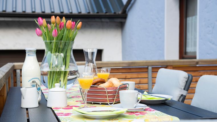 A beautifully set table on a terrace with fresh flowers, milk, and breakfast treats. The atmosphere is inviting and perfect for a relaxing morning.