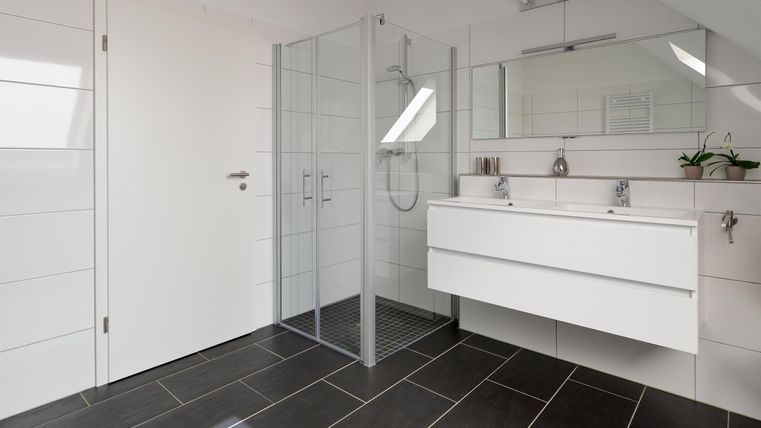 Ein modernes Bad mit weißen Wänden und schwarzen Fliesen. Es verfügt über eine Dusche aus Glas und einen eleganten Waschtisch mit Spiegel.