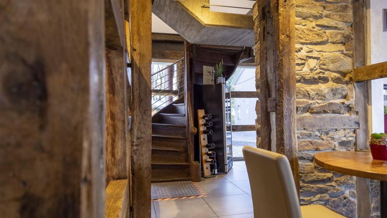 Een gezellige binnenruimte met rustieke houten muren en een trap. Op een tafel staat een kleine plant.