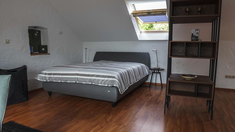 Ein gemütliches Schlafzimmer mit einem großen Bett und einem modernen Regal. Die Dachfenster sorgen für viel Tageslicht.