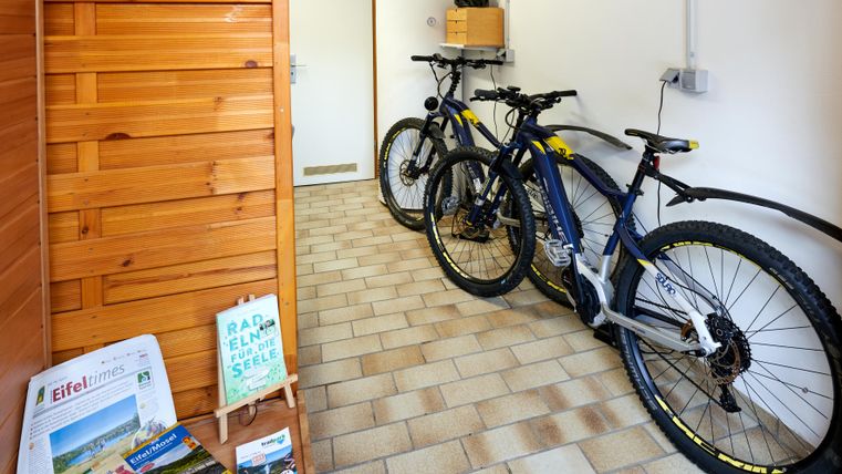 A hallway with two modern mountain bikes and a wooden shelf. Informational materials about the region are hanging on the wall.