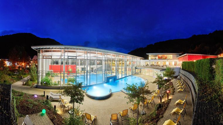 Ein modernes Gebäude mit einem Pool und einer gepflegten Gartenlandschaft. Die Szene ist nachts beleuchtet mit einem klaren Himmel im Hintergrund.