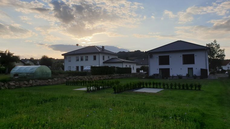 Ein ruhiges ländliches Grundstück mit zwei modernen Wohnhäusern. Im Hintergrund sind Bäume und ein schöner Himmel zu sehen.