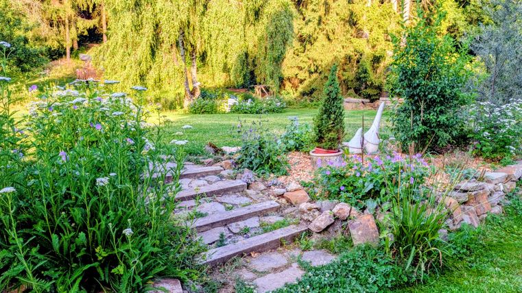 A beautiful garden with colorful flowers and a stone staircase. In the background, green trees and bushes can be seen.