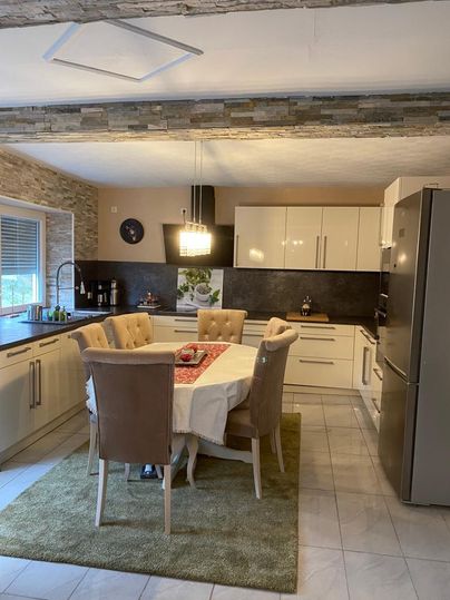 Eine moderne Küche mit einem runden Esstisch und beigen Stühlen. Die Wände sind mit Steinoptik verziert und die Ausstattung ist hell und einladend.