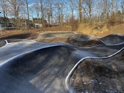 Een gepompte baan met gebogen bochten en een heldere blauwe lucht. De omgeving is omringd door bomen en ziet er rustig uit.