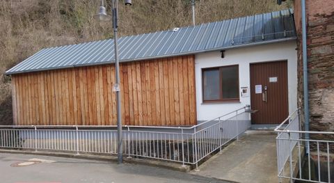 Ein modernes Gebäude mit Holzfassade und einem Flachdach. Es hat eine barrierefreie Eingangstür und befindet sich in einer ländlichen Umgebung.