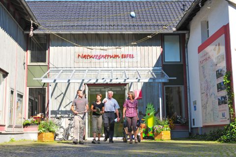 A visitor center with several people standing in front of the entrance. The facade is bright and friendly, surrounded by plants.
