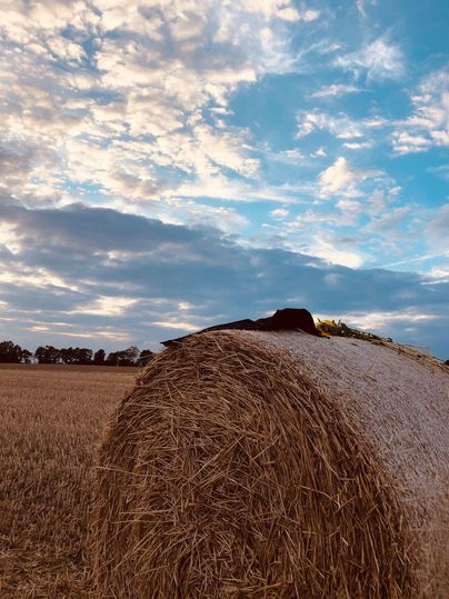 A large hay bale stands in a field under a vast, cloudy sky. The colors of the sky shift between blue and gray, creating a calm atmosphere.