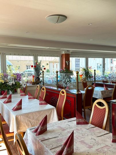 Een restaurant met mooi gedekte tafels. De ramen laten veel licht binnen en er zijn planten en decoraties op de achtergrond.