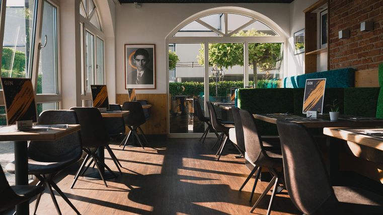 Ein modernes Restaurant mit Holzfußboden und gemütlichen Tischen. Durch große Fenster fällt sanftes Licht auf den Raum.