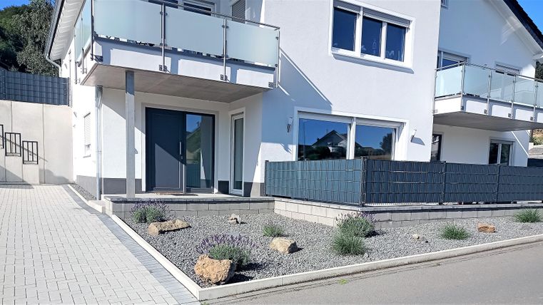 Een modern huis met een lichte buitenruimte. De entree is schoon ontworpen, omringd door kleine planten en stenen.