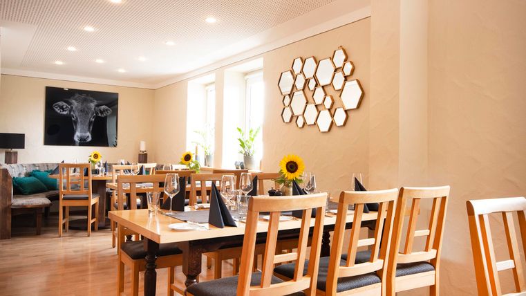 An inviting restaurant with wooden chairs and tables. Decorative mirrors and a cow graphic hang on the wall.
