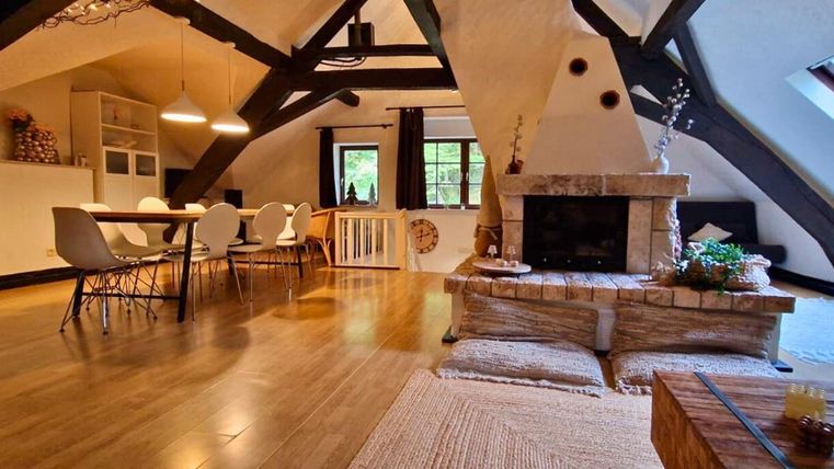 A modern and stylish living room with wooden beams and a cozy fireplace. The room is brightly lit and has an inviting dining area with a large table.