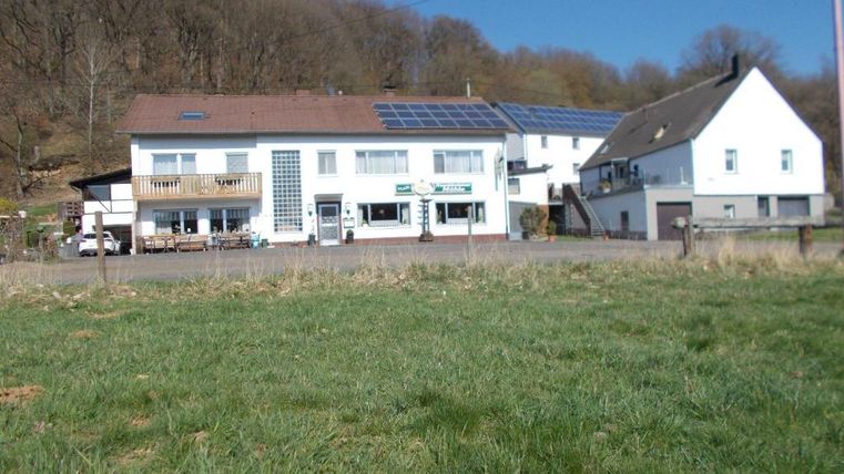 Ein charmantes Gebäude in ländlicher Umgebung mit einem grünen Rasen. Im Vordergrund sind Wiesen zu sehen, und im Hintergrund befinden sich Bäume.