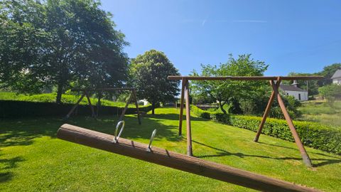 Een mooie speeltuin met schommels op een groen veld. De lucht is helder en blauw, omringd door bomen.