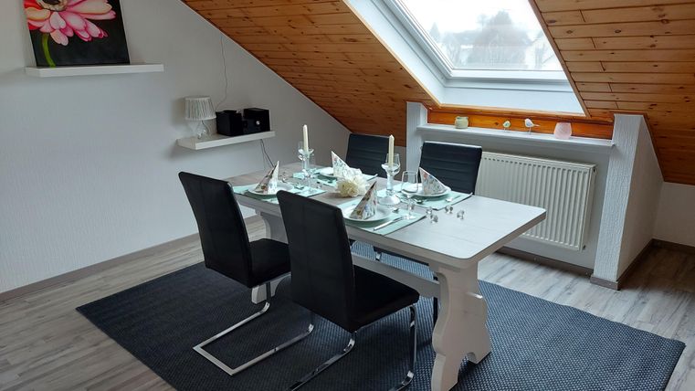 A modernly designed dining area with a table and black chairs. The skylight lets in plenty of light, and a floral painting adorns the wall.