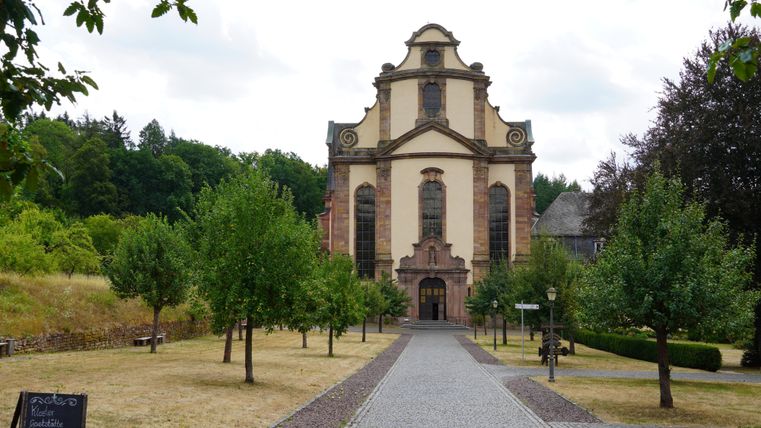 Eine beeindruckende Kirche steht am Ende eines gepflasterten Weges. Umgeben von Bäumen und Grünflächen strahlt sie eine ruhige Atmosphäre aus.
