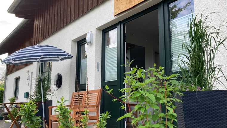 Ein einladendes Haus mit einer Terrasse. Auf der Terrasse stehen Holzstühle und Pflanzen in Töpfen.