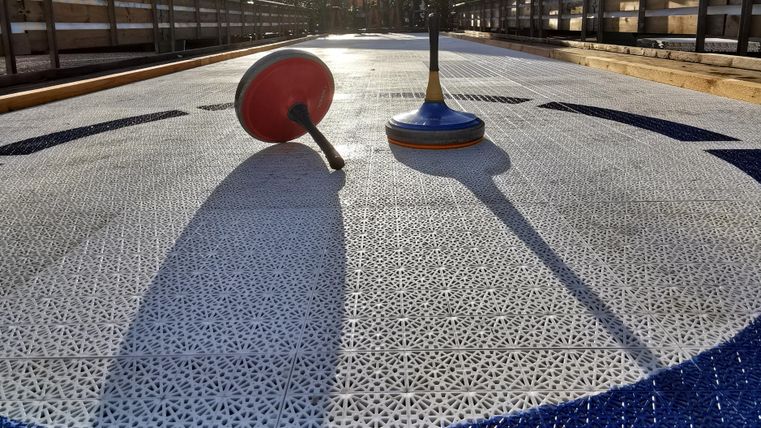 Zwei Kreisel liegen auf einer strukturierten Spieloberfläche. Die Sonne wirft lange Schatten und die Atmosphäre ist lebhaft.