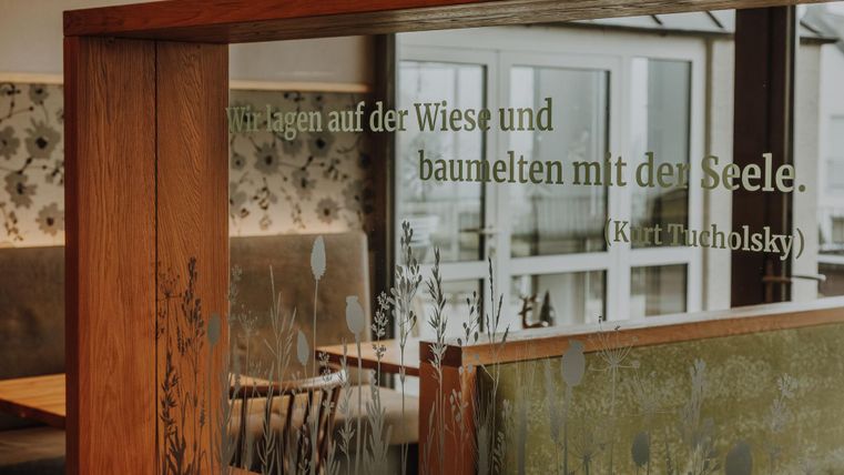 Ein gemütliches Restaurant-Ambiente mit Holzverkleidung und eleganter Floraldarstellung. Ein Zitat von Kurt Tucholsky schmückt die Wand.