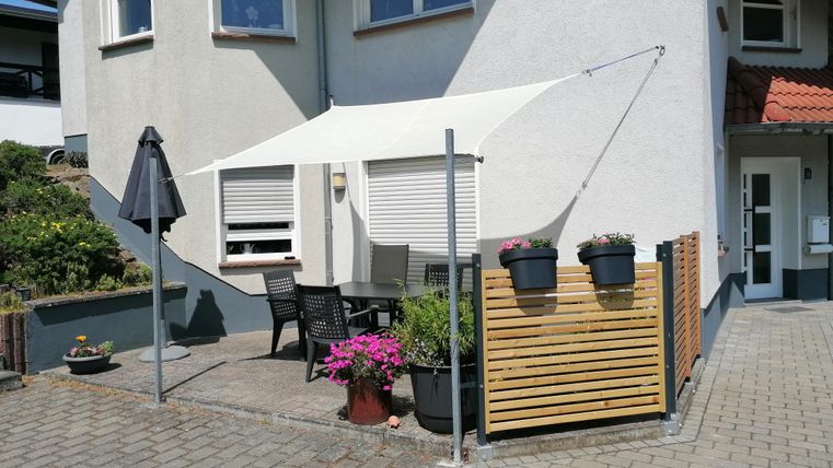 Een gezellige buitenruimte met een witte zonnescherm en terrasmeubels. Bloemen in potten vullen de uitnodigende sfeer aan.