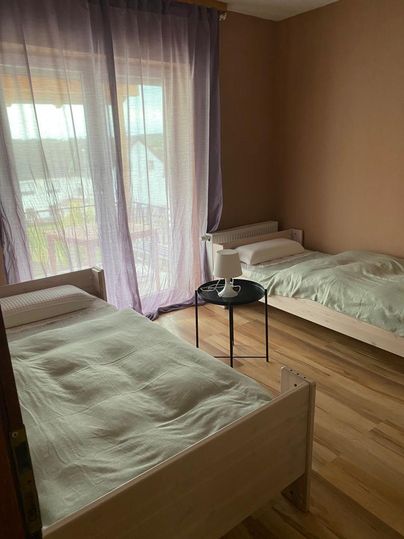 Ein Schlafzimmer mit zwei Einzelbetten und einem kleinen Tisch. Große Fenster mit lila Vorhängen lassen viel Licht herein.