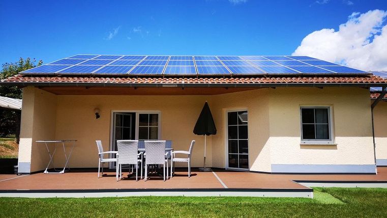 Een modern huis met zonnepanelens op het dak en een gezellige buitenruimte. Het groene gras en de blauwe lucht zorgen voor een prettige sfeer.