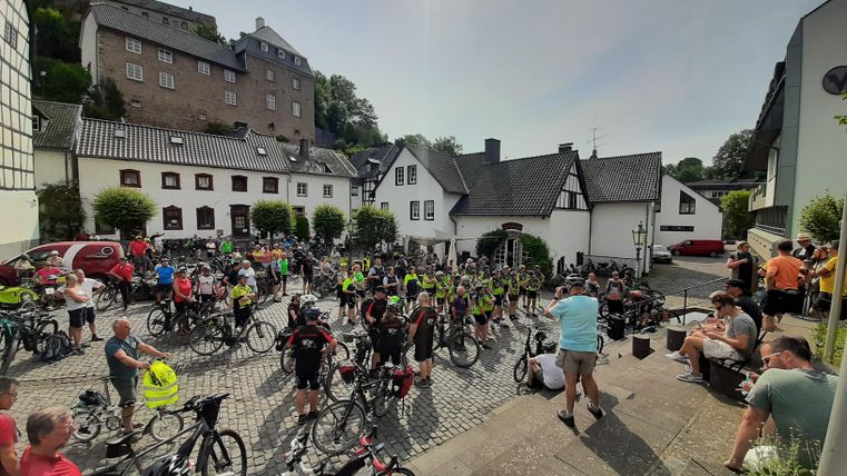 Eine Menge von Radfahrern versammelt sich auf einem Platz mit historischen Gebäuden. Die Atmosphäre ist lebhaft und es sind viele Fahrräder zu sehen.