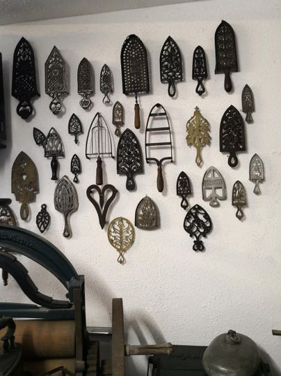 Eine Wand mit einer Sammlung von antiken Eisen. Die verschiedenen Formen und Größen zeigen die Vielfalt historischer Bügeleisen.