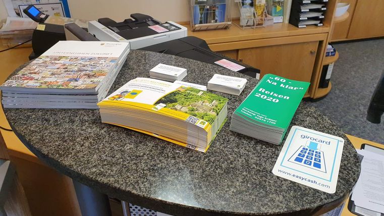 Ein Empfangstresen mit verschiedenen Informationsmaterialien. Darunter befinden sich Broschüren, Kataloge und eine grüne Informationsschrift.