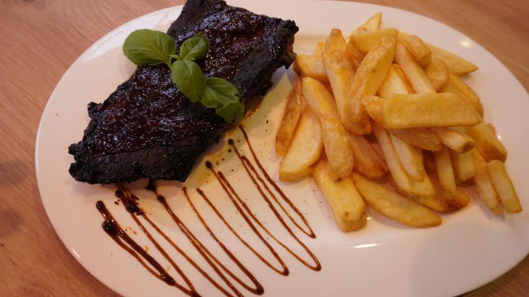 A plate with grilled meat and crispy fries. The meat is garnished with a dark sauce and fresh basil.