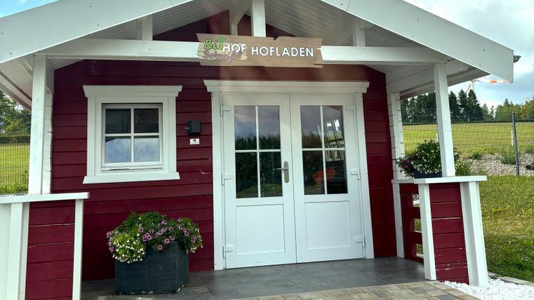 A red wooden house with a white roof and an inviting front door. In front of the house, there are plants in pots, and the area is well-maintained.
