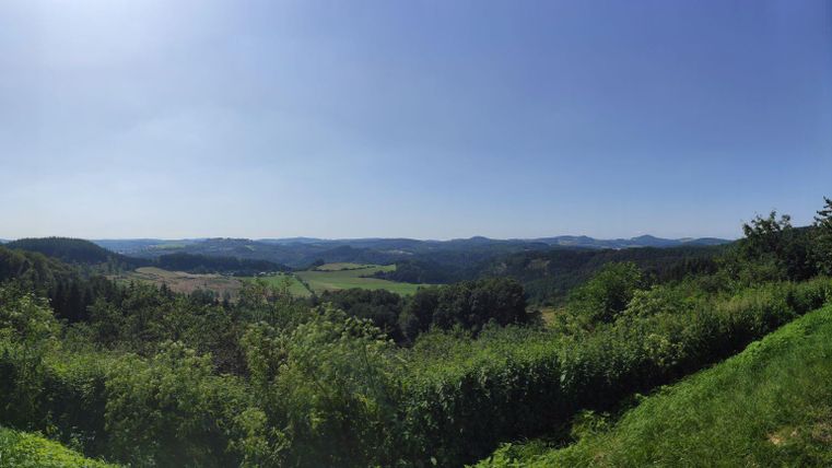 Eine weitläufige Landschaft mit sanften Hügeln und viel grünem Bewuchs. Der Himmel ist klar und strahlend blau.