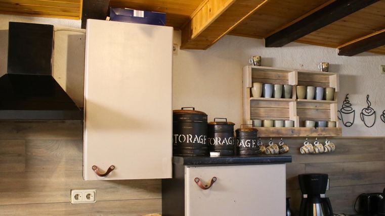 A cozy kitchen with wooden shelves and decorative coffee mugs. Kitchen appliances and storage containers are on the countertop.