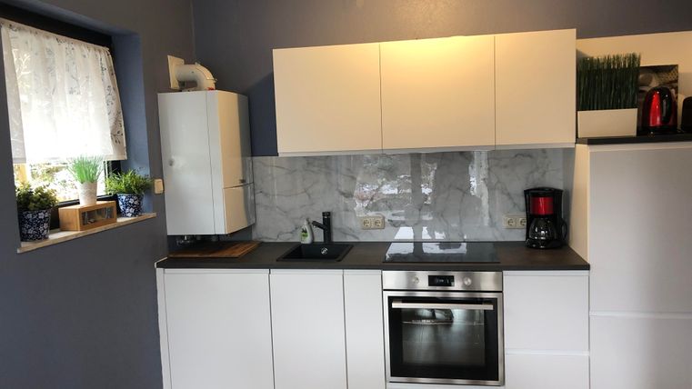 Een moderne keuken met witte kasten en een elegante keukenwerkplek. De muren zijn geschilderd in een zachte blauwtint, en vensters met gordijnen laten daglicht binnen.