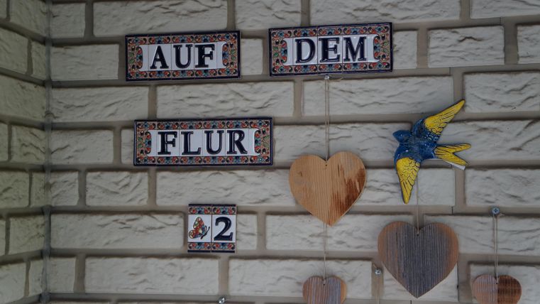 A wall with decorative signs showing "In the hallway 2". Next to it, wooden hearts and a colorful bird figure are hanging.