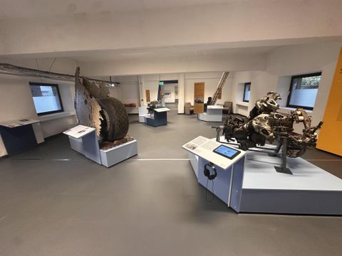 Ein Ausstellungsraum mit verschiedenen technischen Objekten und Informationalständen. Die Objekte sind auf Podesten angeordnet und zeigen interessante Maschinenbauteile.