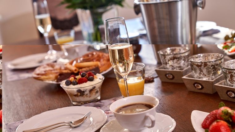 A beautifully set table with various breakfast treats. There is champagne, fresh fruit, and a cup of coffee.