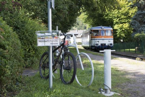 A bicycle is standing at a parking spot with a sign for the bike path. In the background, a train is passing by.