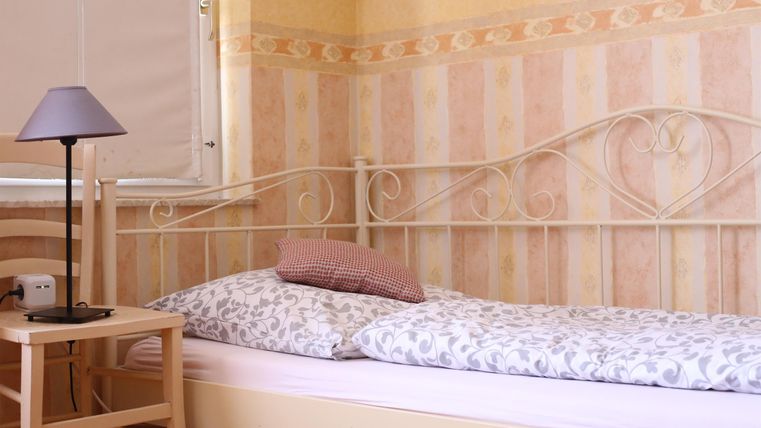 Ein gemütliches Schlafzimmer mit einem Einzelbett und einer kleinen Lampe auf einem Nachttisch. Die Wände sind in sanften Farben gehalten.