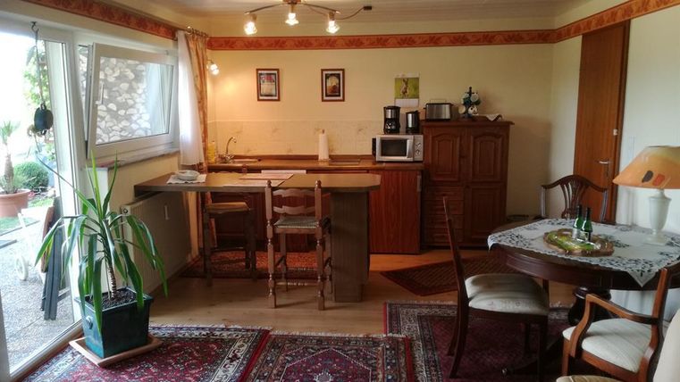 Eine helle, gemütliche Küche mit einem Essbereich. Der Raum ist mit einem Teppich und Pflanzen dekoriert.