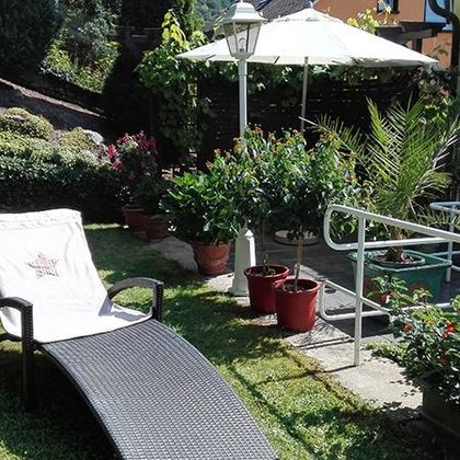 Ein ruhiger Garten mit Sonnenliege, einem Sonnenschirm und blühenden Pflanzen. Die grüne Umgebung lädt zum Entspannen ein.