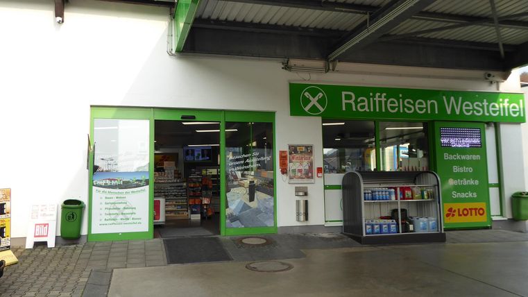 A market with an entrance area in green colors. Billboards and shelves are visible, displaying various products.