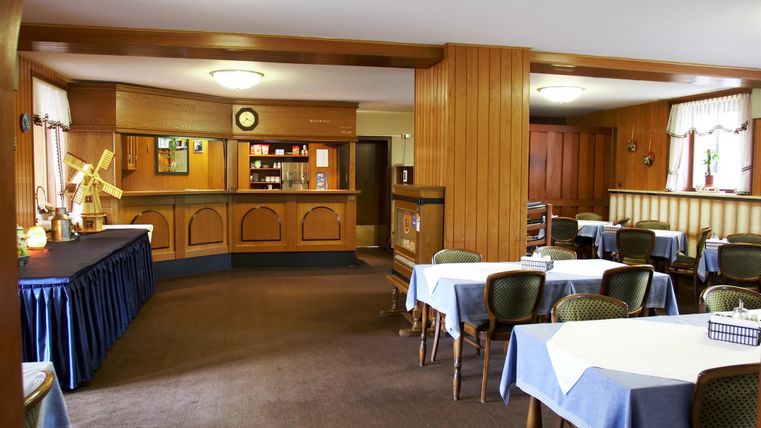 A cozy dining area with wooden walls and round tables. On the table are blue tablecloths and in the background there is a counter.