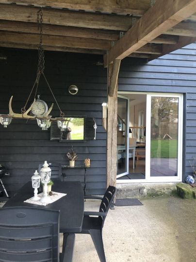 Ein moderner Außenbereich mit einem schwarzen Tisch und Stühlen. Im Hintergrund sieht man eine große Glasschiebetür, die zum Innenraum führt.