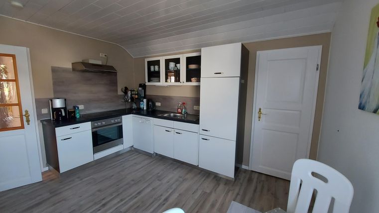 A modern kitchen with white furniture and wooden flooring. The room is bright and well-furnished, with modern appliances.